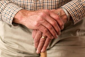 Older man with hands clasped holding a walking stick